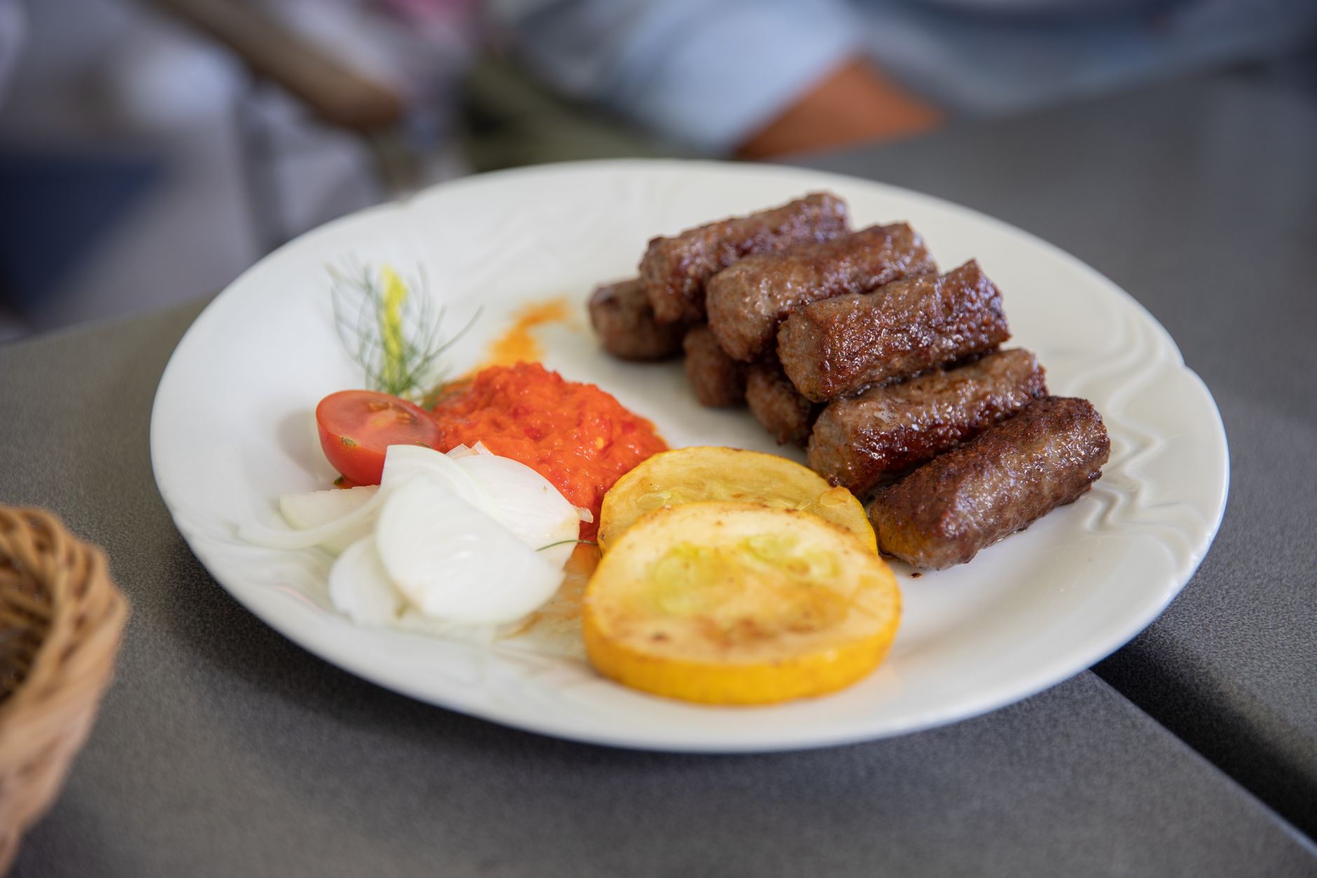 Чевапчичи с луком, свежими овощами и красным перечным соусом — классический заказ в сербской чевапджинице